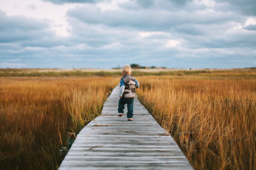 young boy running with a backpack on long flat trail made of wood