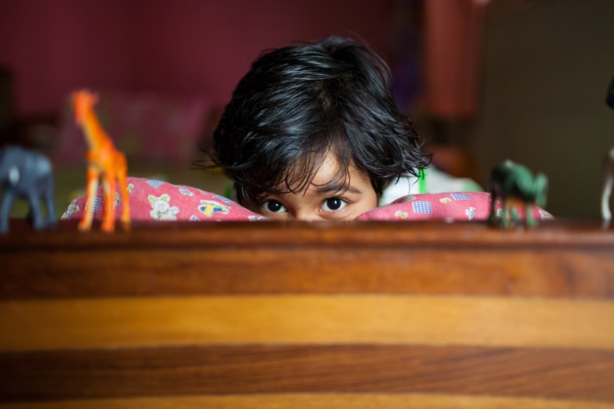 boy peaking holding a pillow looking at his plastic toys