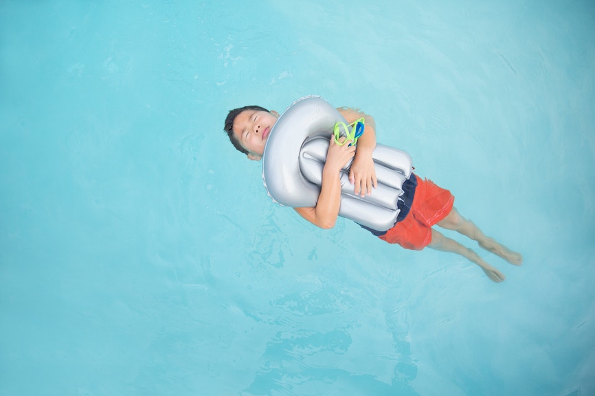 boy in pool oh his back holding a floatie