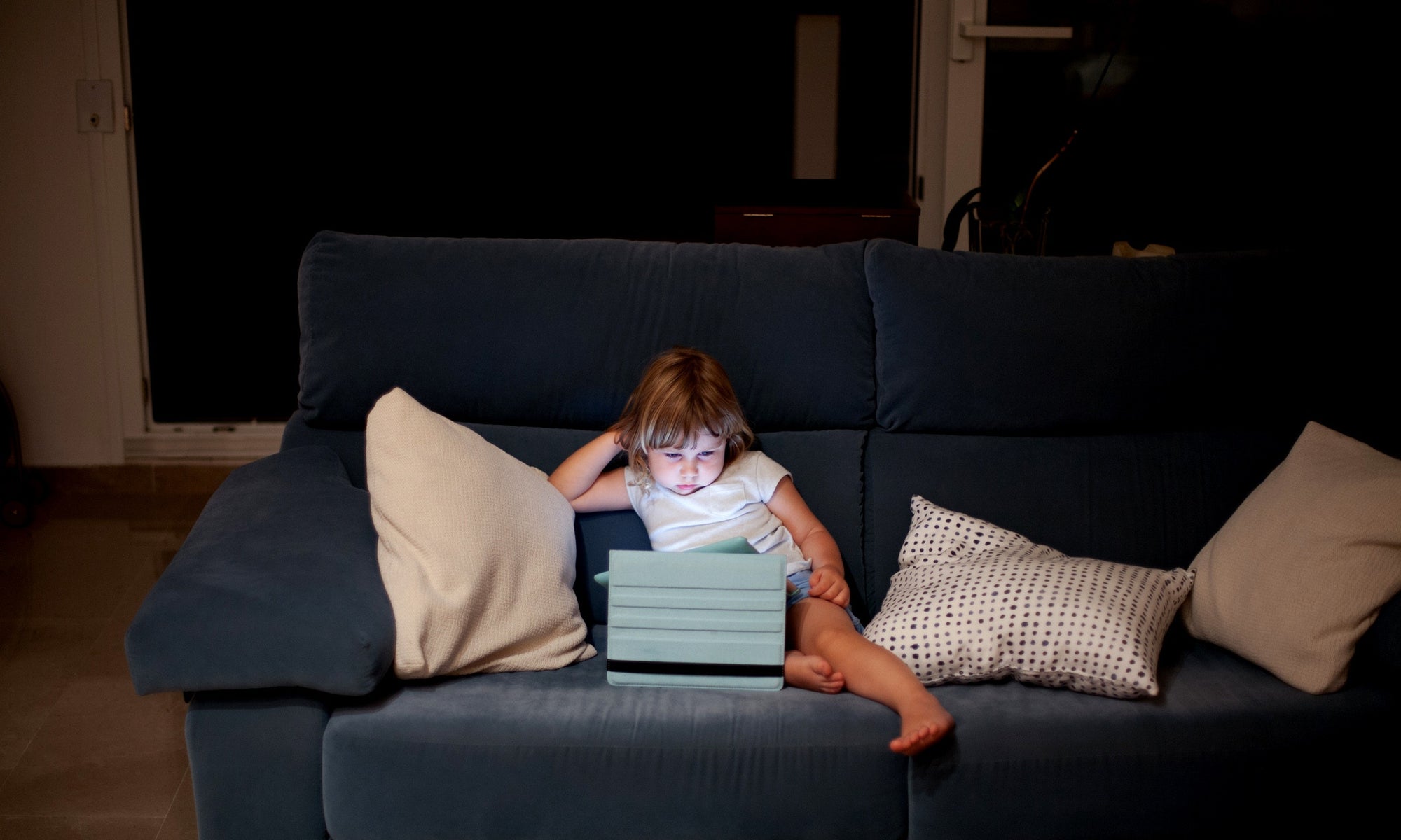 little girl sitting on sofa watching movie on tablet