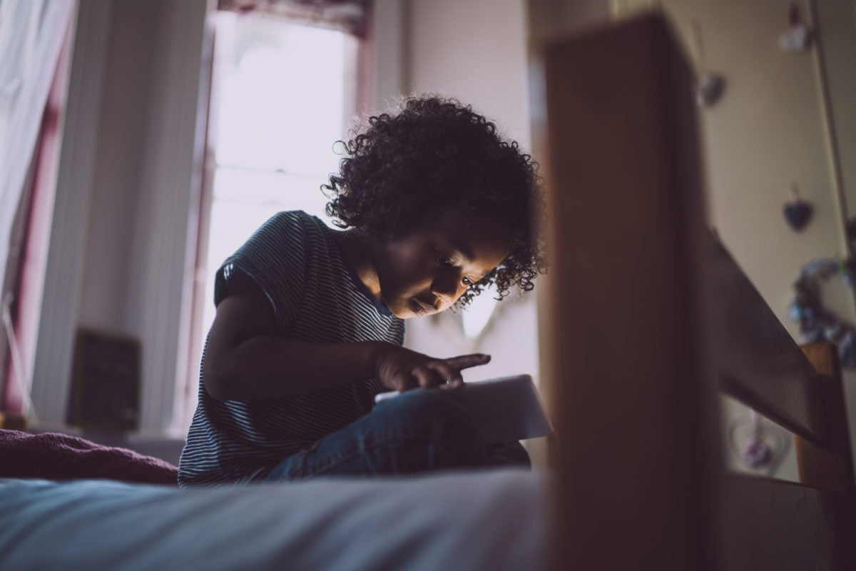 Little girl sitting with mobile phone on bed at home