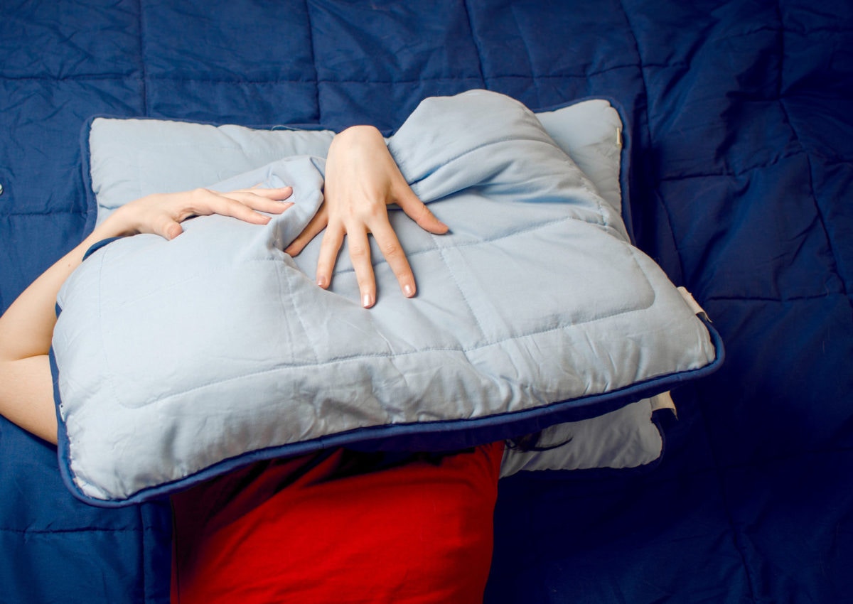 Lady cover her head by pillow on a bed