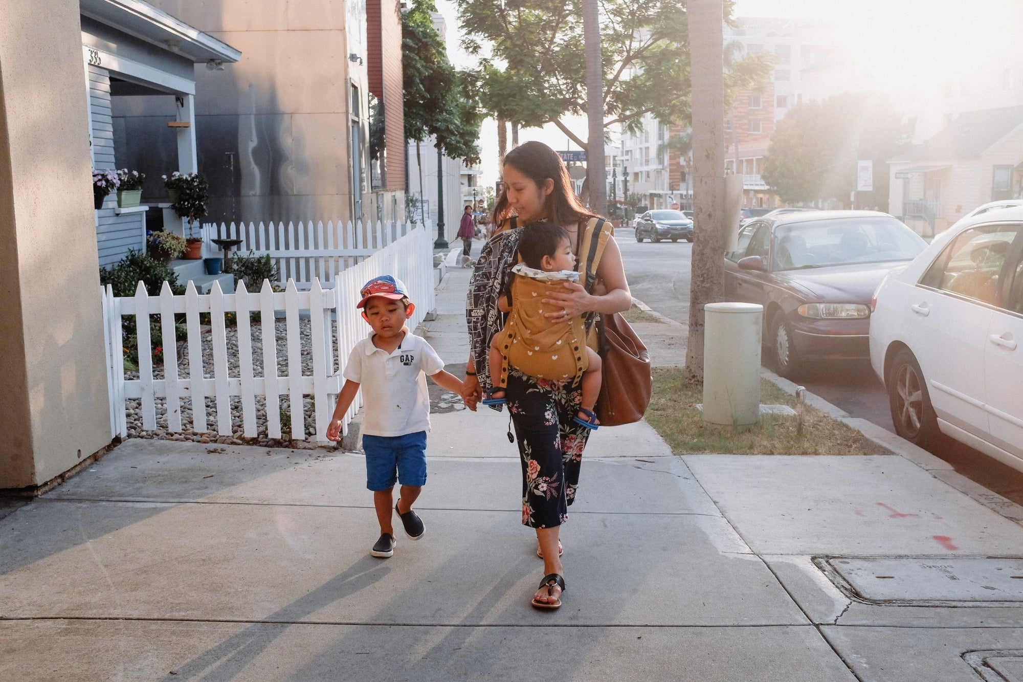 mom holing hands of one child the other in a bjorn