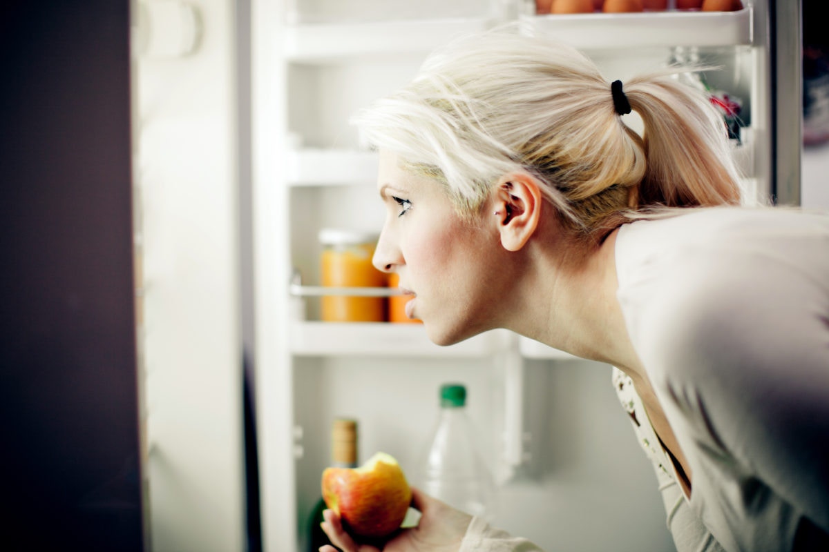 woman holding an apple looking in the refrigerator