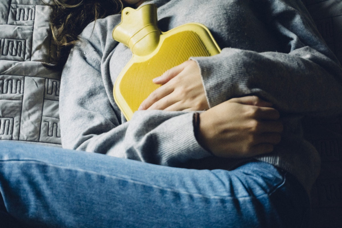 young woman is lying on the bed with hot water bottle, have stomach ache