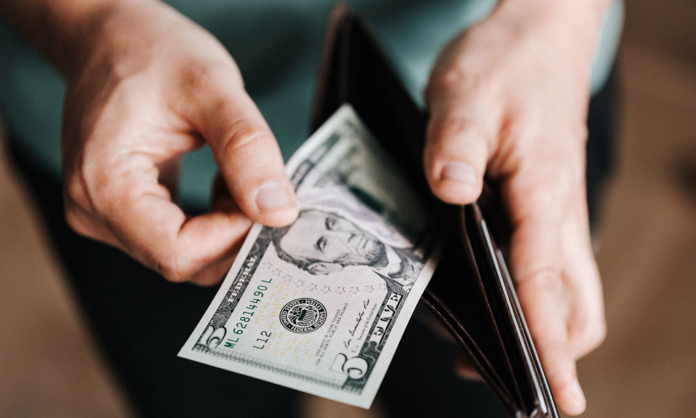 man holding wallet with five dollars